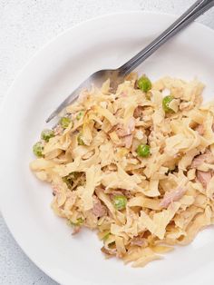 a white plate topped with pasta and peas next to a fork on top of a table