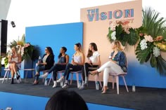 four women sitting on chairs in front of a blue and pink wall with the vision summit logo