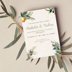 an elegant wedding card with olives and greenery is displayed on top of a table