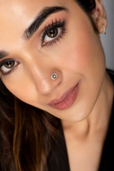 a close up of a woman with eyeliner and piercings on her nose looking at the camera