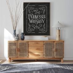 a wooden sideboard with two vases on top and a framed poster above it