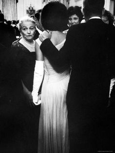 black and white photograph of woman in evening dress with man standing next to her looking on