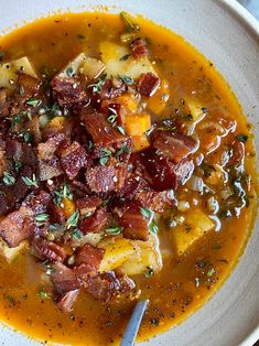 a white bowl filled with soup topped with bacon and potatoes on top of a table