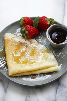 pancakes with powdered sugar and strawberries on a plate next to a cup of syrup