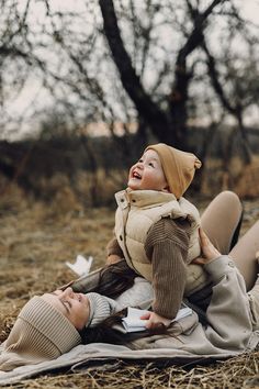 a woman sitting on the ground with a baby in her lap and another person laying down next to her