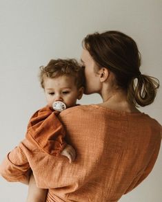 a woman holding a baby in her arms and kissing it's face with the other hand