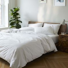 a bed with white sheets and pillows next to a potted plant in the corner