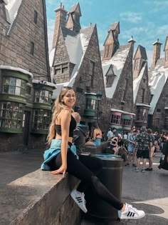 a woman sitting on the edge of a wall in front of a castle like building