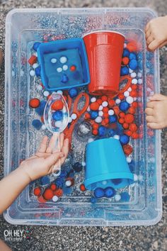 two children playing with red, white and blue plastic objects in a play tray on the ground