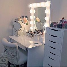 a white vanity with lights on it and a chair in front of the mirror that is lit up