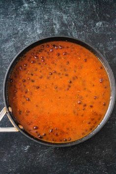 a pot filled with red sauce sitting on top of a black counter next to a knife