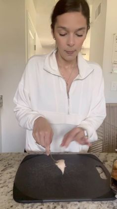 a woman in white shirt preparing food on top of a black tray