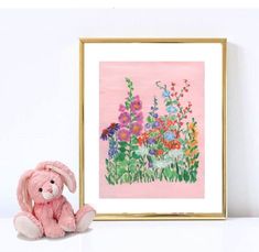 a pink teddy bear sitting next to a painting on a white wall with flowers in the background