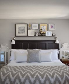 a bed with white and gray pillows, framed pictures on the wall above headboard