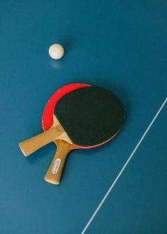 two ping pong paddles and a white ball on a blue table