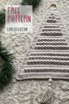 a crocheted christmas tree ornament hanging on a wall with pine needles