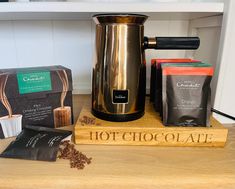 an electric coffee maker sitting on top of a wooden table next to two bags of coffee