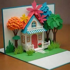 a card with a house made out of paper and flowers on the front, sitting on a table