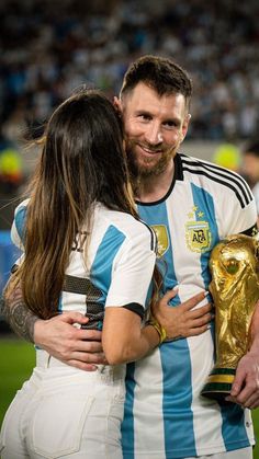 a man and woman hugging each other while holding a soccer trophy in front of a crowd