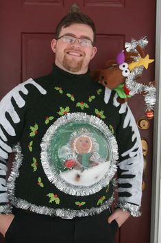 a man standing in front of a red door wearing a ugly sweater with a christmas tree on it