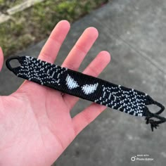 a hand holding a black and white beaded bracelet with an evil face on it