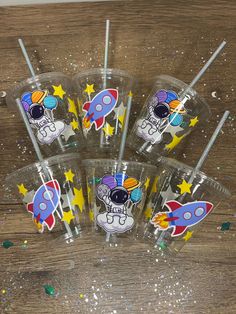 six space themed cups with straws in the shape of rockets and stars on them