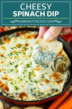 a hand dipping cheese into a skillet filled with spinach dip surrounded by carrots and bread