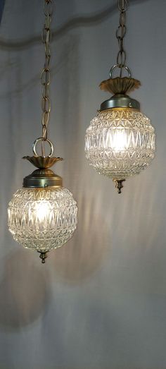 two glass lamps hanging from chains on a wall