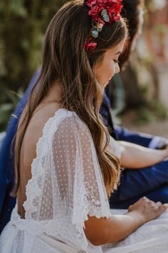 a woman sitting on the ground wearing a white dress with red flowers in her hair