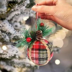 a hand holding a plaid christmas ornament in front of a decorated christmas tree