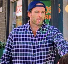 a man standing in front of a store with his hands out to the side while wearing a blue and white checkered shirt