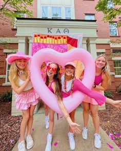 three girls in pink dresses holding up a heart shaped balloon