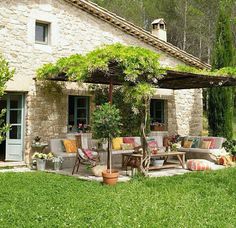 an outdoor patio with chairs and tables in front of a stone building surrounded by greenery