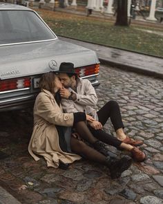 a man and woman sitting next to each other on the ground near a parked car