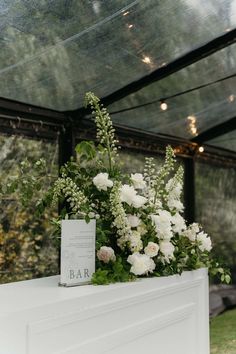 white flowers and greenery sit on top of a fireplace mantel in a glass walled room