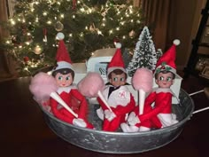 four elfs sitting in a bucket with candy canes on the table next to a christmas tree