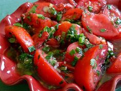 a red bowl filled with sliced tomatoes and herbs