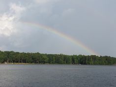 a rainbow in the sky over a body of water with trees and houses on it