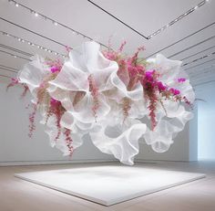 a large white sculpture with pink flowers hanging from it's sides in an empty room