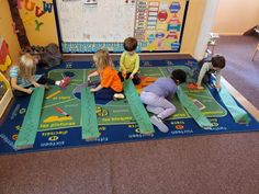 there are children sitting on the floor in front of a bulletin board and playing with construction paper