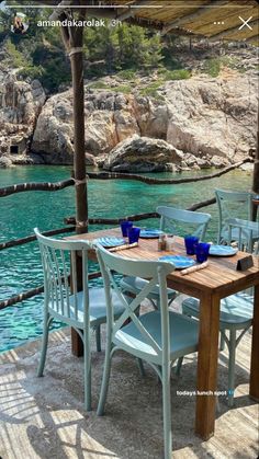 an outdoor dining table with blue chairs and umbrella over it on the deck overlooking water