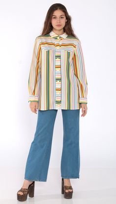 "Vintage 70s shirt in white with rainbow stripes. Buttons down the chest with long sleeves and a collar. Every garment we sell is authentic vintage and one-of-a-kind! You will receive the exact item photographed. Condition: Very good vintage. Best fits women's: Small to medium Material: Feels like Polyester MEASUREMENTS Taken from seam to seam while the garment is lying flat. Double the armpit, waist, and hips For reference, model is 5'5\" and measures 32-24-34. Length from Top: 27\" Armpit to A Retro Rainbow Tops For Spring, Retro Long Sleeve Top With Striped Collar, Retro Spring Top With Rainbow Print, Retro Rainbow Print Top For Spring, Vintage Multicolor Shirt With Buttons, Vintage Multicolor Tops With Button Closure, Retro Multicolor Tops With Button Closure, Multicolor Long Sleeve Vintage Blouse, Multicolor Long Sleeve Top With Vertical Stripes