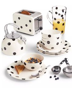 polka dot dishes and cups are arranged on a white surface with spoons, tea kettle, toaster, and coffee pot