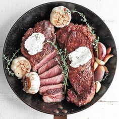 steak with garlic and mushrooms in a cast iron skillet on a white wooden table