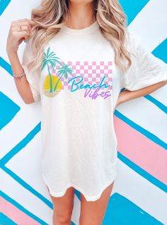 "Looking for a comfy tee that captures the essence of summer? Look no further. Featuring a retro-style script font that reads \"Beach Vibes,\" enhanced by a beautifully illustrated palm tree and sunset on the side, adding a touch of tropical paradise to the overall aesthetic. The pink checkered pattern in the background adds a pop of color and a playful touch to the design. With its Coconut Girl-inspired aesthetic and retrowave vibes, this tee is a throwback to the more carefree summer days of t Beachy Summer, Pink Checkered, Inspired Aesthetic, Aesthetic Shirt, Vaporwave Aesthetic, Coconut Girl, Aesthetic Shirts, Comfort Colors Tee, Summer Tee