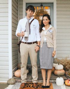 a man and woman holding hands standing in front of a house with pumpkins on the porch