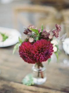 a vase filled with red flowers sitting on top of a wooden table next to plates