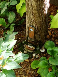 a small gnome's house in the woods next to a tree and some plants