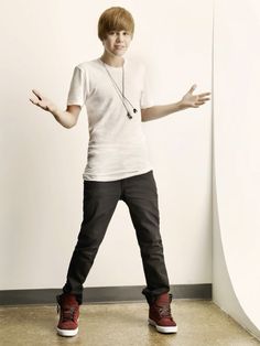 a young man standing in front of a white wall with his hands out to the side