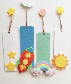 three felt bookmarks with different designs and colors on them, one has a rocket ship, the other is a rainbow